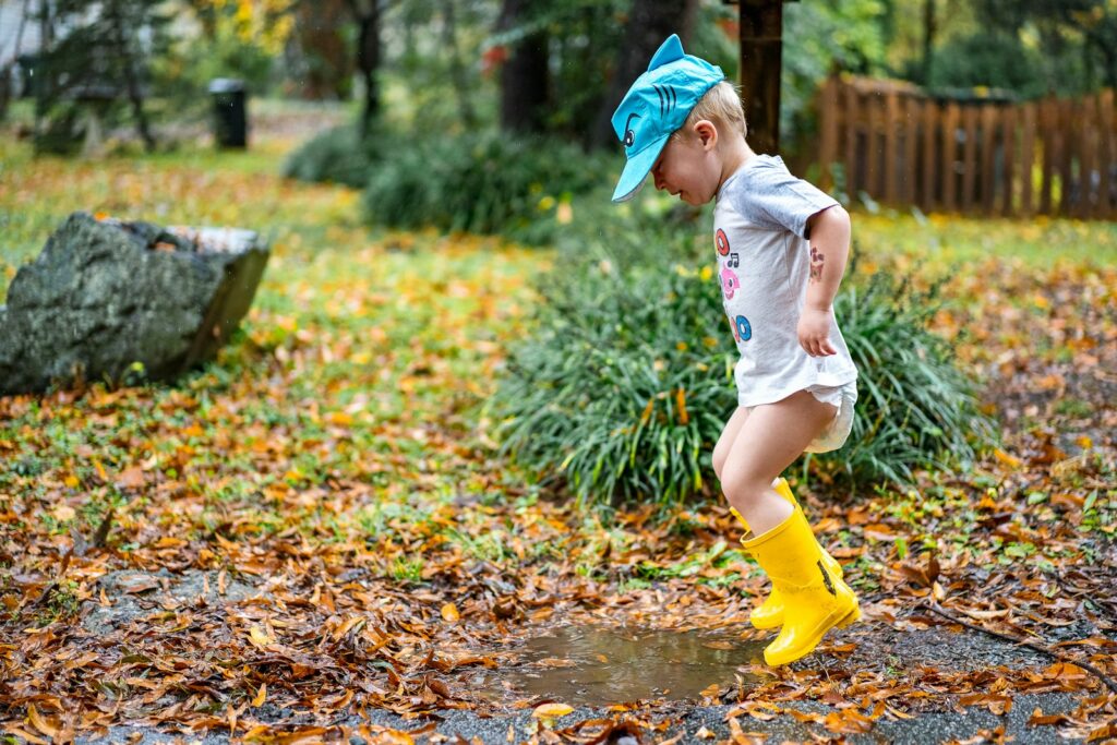 Enfant en bottes jaunes sautant dans une flaque lors d'une sortie sous la pluie